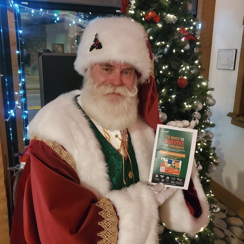 Santa holding a Christmas book beside a decorated tree