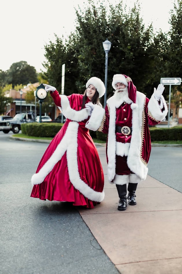Santa and Mrs. Claus waving while crossing a downtown street